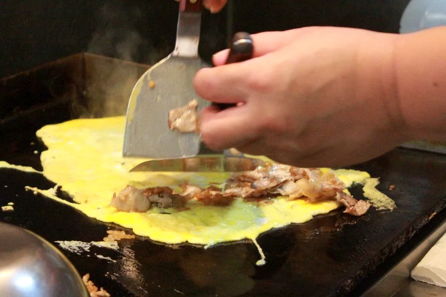 鉄板で卵と肉を焼く手元。湯気が出ている